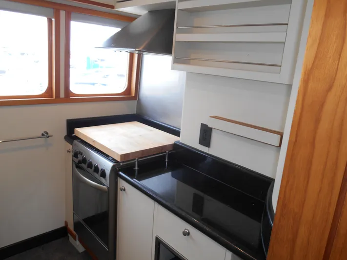 Suspense Yacht Photos Pics Compact kitchen in a 2005 Inace Trawler with stove, cutting board, and black countertops.
