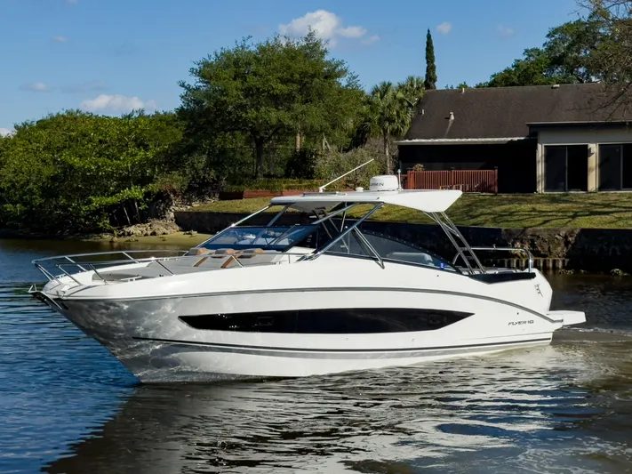  Yacht Photos Pics 2024 Beneteau Flyer 10 boat cruising on a calm river near a house.