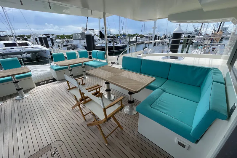 Firefly Yacht Photos Pics Luxurious 2018 Serenity 64 yacht deck with turquoise seating and wooden tables at marina.