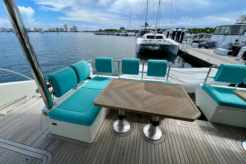 Firefly Yacht Photos Pics Luxurious Serenity 64 yacht deck with turquoise seating and wooden table, docked at marina.