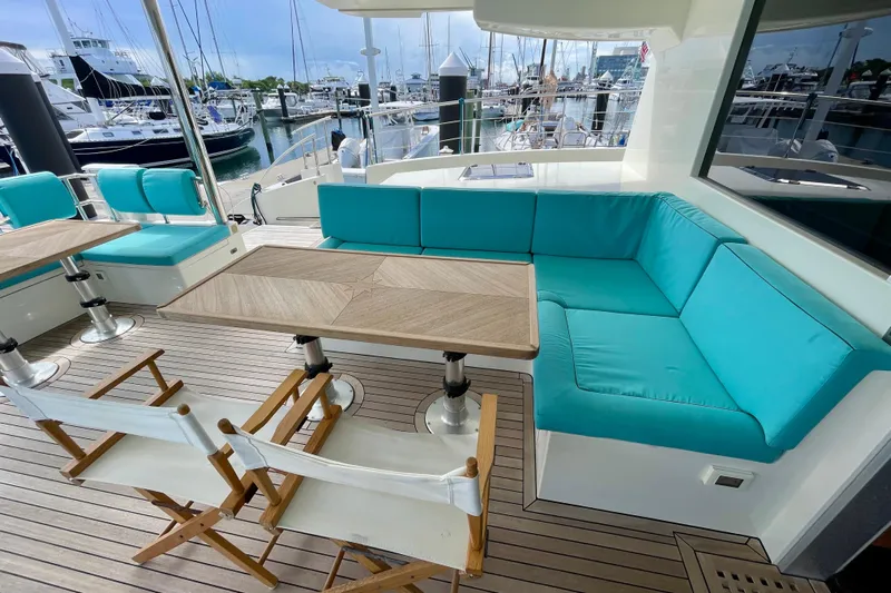 Firefly Yacht Photos Pics Luxurious Serenity 64 yacht deck with turquoise seating and wooden tables, docked at a marina.