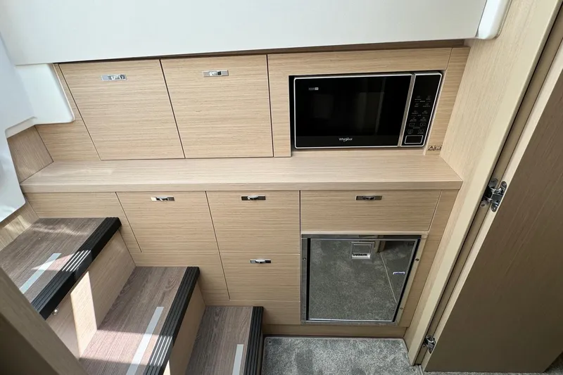  Yacht Photos Pics 2026 Jeanneau DB/37 IB interior with wooden cabinetry, microwave, and compact refrigerator.