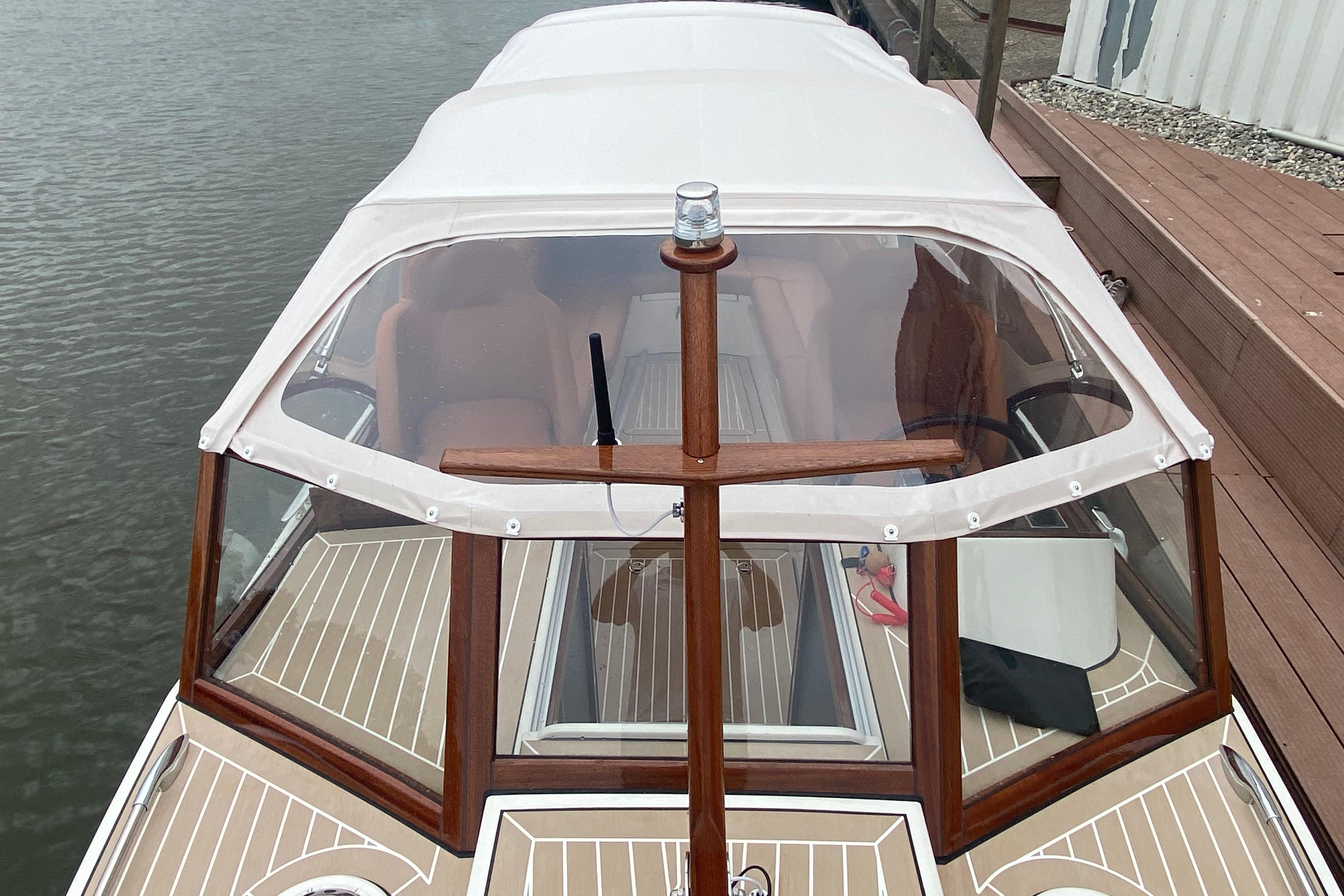 2022 STATEMENT MARINE PTS 26 boat with white canopy and wooden accents docked by water.