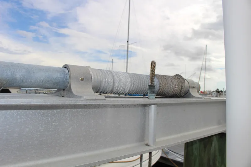  Yacht Photos Pics Close-up of a metal cable mechanism on a dock, with boats in the background.