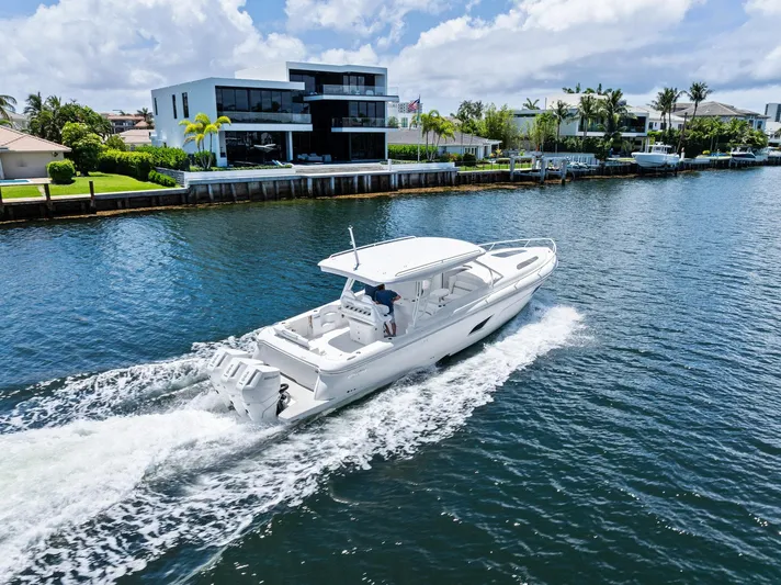  Yacht Photos Pics 2024 Intrepid 41 Valor cruising on a sunny waterfront near modern homes.