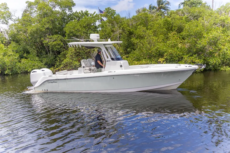 Yacht Photos Pics 2023 Edgewater 262CC boat cruising on a calm river, surrounded by lush greenery.