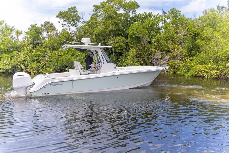  Yacht Photos Pics 2023 Edgewater 262CC boat cruising on a serene waterway surrounded by lush greenery.