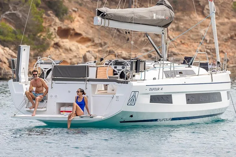  Yacht Photos Pics 2025 Dufour 41 yacht with two people relaxing on deck in a scenic coastal setting.