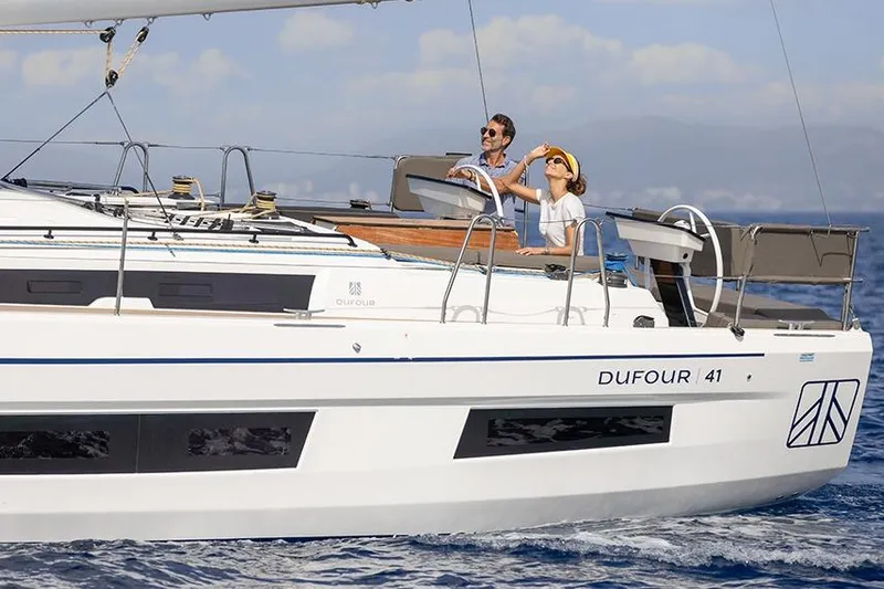  Yacht Photos Pics 2025 Dufour 41 sailboat cruising with two people on deck, enjoying the ocean view.