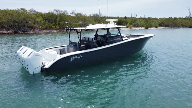  Yacht Photos Pics 2023 Yellowfin 42 boat on calm water near a lush shoreline.
