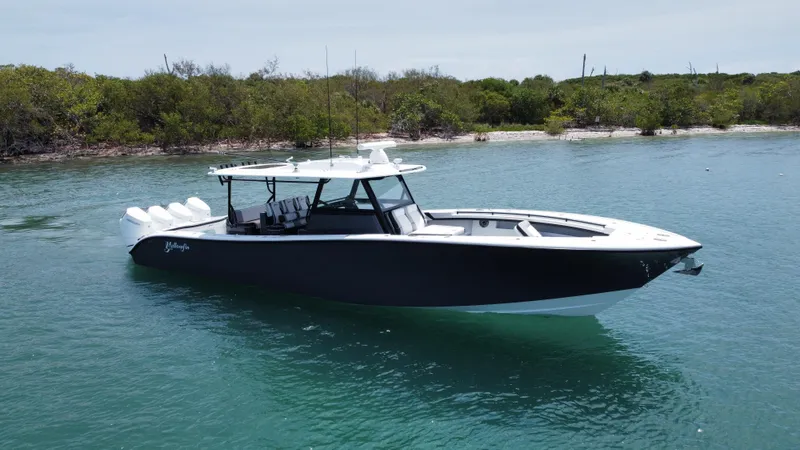  Yacht Photos Pics 2023 Yellowfin 42 boat on calm water near a lush shoreline.