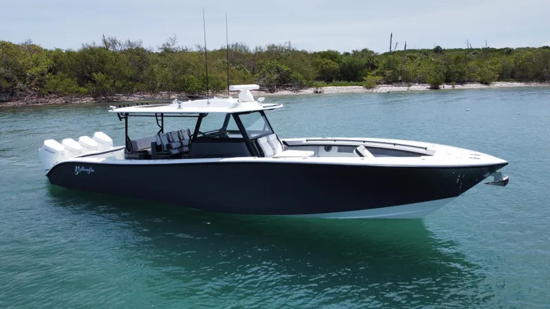  Yacht Photos Pics 2023 Yellowfin 42 boat on calm water near a lush shoreline.