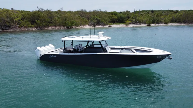  Yacht Photos Pics 2023 Yellowfin 42 boat on calm water near a lush shoreline.