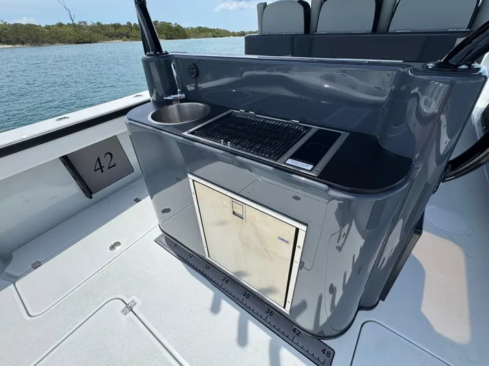  Yacht Photos Pics 2023 Yellowfin 42 boat with sleek outdoor kitchen and sink, set against a serene water backdrop.