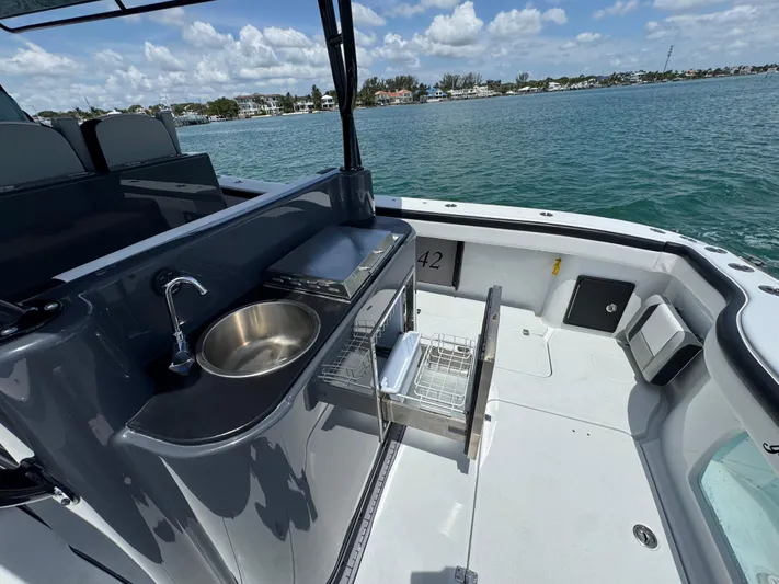  Yacht Photos Pics 2023 Yellowfin 42 boat deck with sink and storage, overlooking calm waters and distant shoreline.