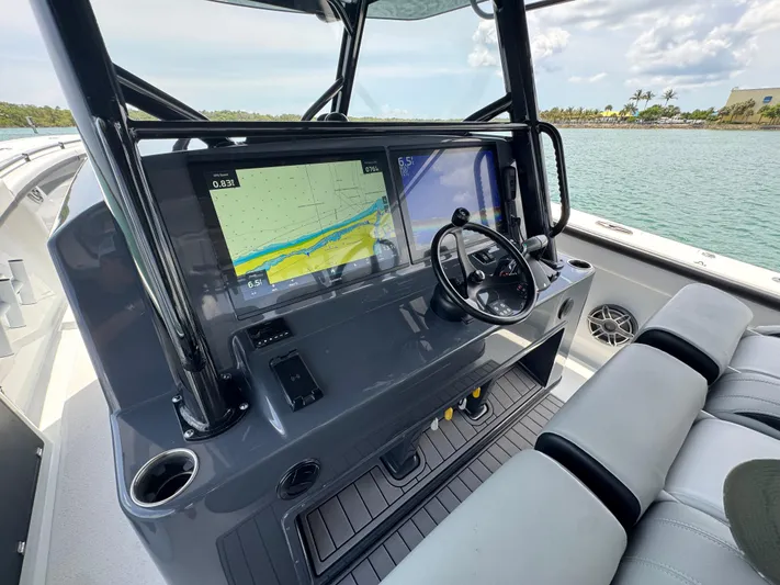  Yacht Photos Pics 2023 Yellowfin 42 boat dashboard with navigation screens and steering wheel, overlooking calm waters.
