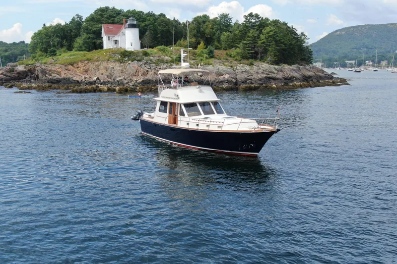 Minkie B Yacht Photos Pics 1997 Lyman-Morse Custom Flybridge yacht near rocky shoreline with lighthouse in background.