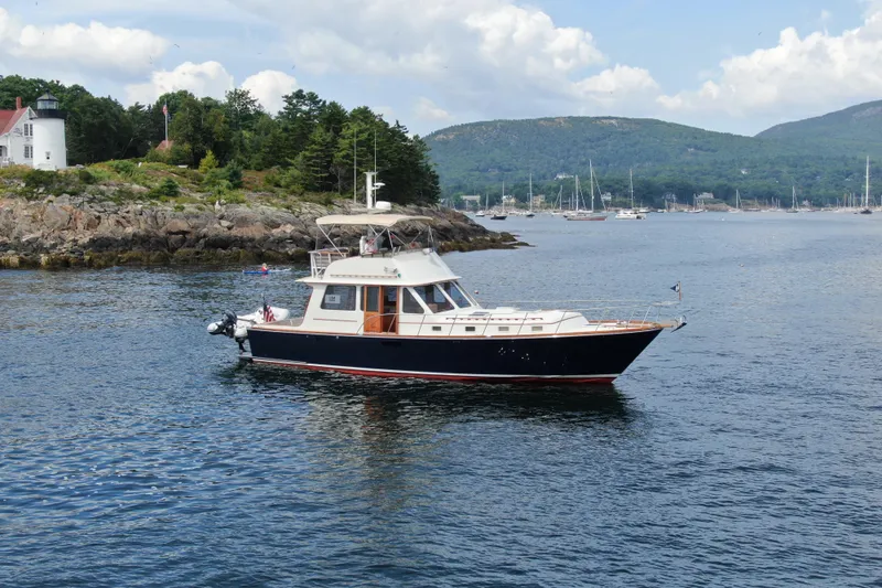 Minkie B Yacht Photos Pics 1997 Lyman-Morse Custom Flybridge yacht cruising near rocky shoreline and lighthouse.