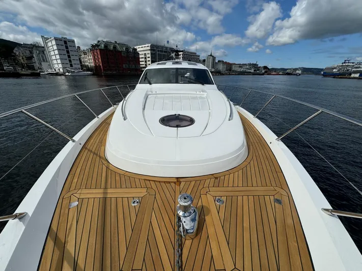  Yacht Photos Pics 2009 Princess V65 yacht with teak deck, docked in a scenic harbor under a cloudy sky.