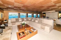 Luxurious yacht interior with beige sofas, wooden ceiling, and ocean view through large windows.