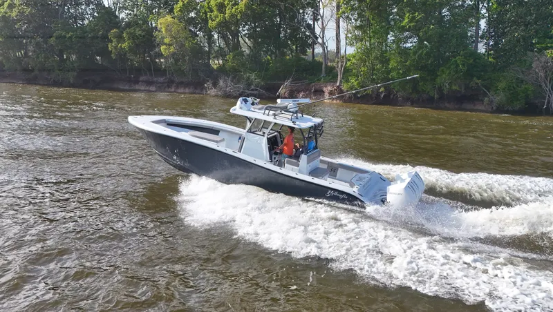Engine Warranty X Trailer Yacht Photos Pics 2022 Yellowfin 34 boat cruising on a river with lush green trees in the background.
