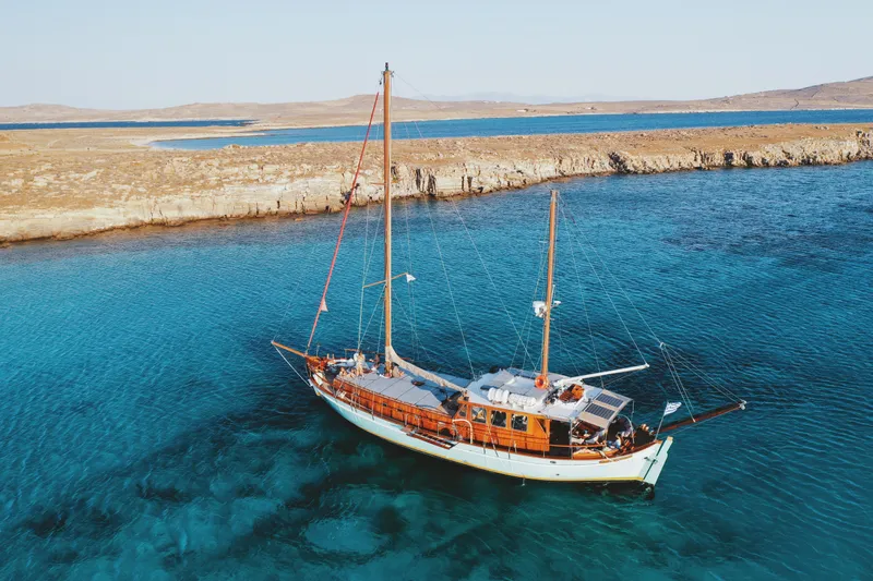 Kaiki Yacht Photos Pics Traditional Greek sailing yacht from 1974 on clear blue waters near rocky coastline.