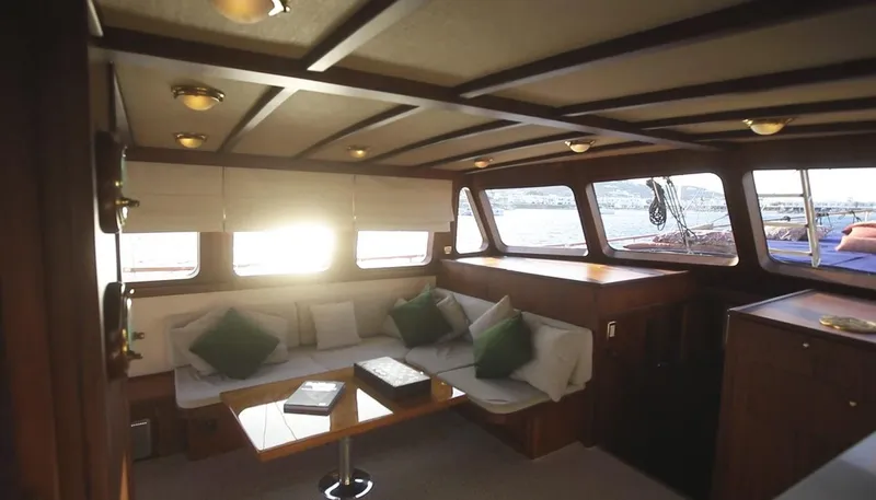 Kaiki Yacht Photos Pics Interior of a 1974 Greek traditional sailing yacht with cozy seating and sunlight streaming through windows.
