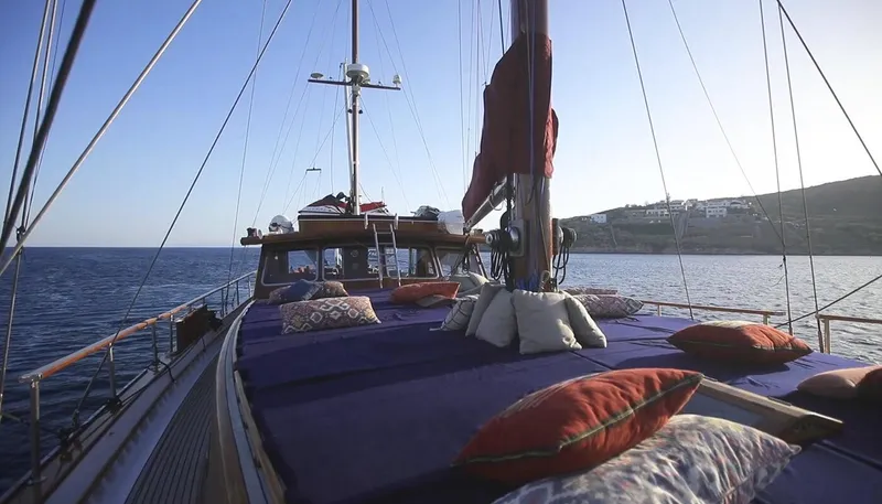 Kaiki Yacht Photos Pics Traditional Greek sailing yacht deck with cushions, 1974 model, cruising near a coastal landscape.