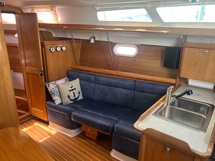Dream Weaver Yacht Photos Pics Interior of 2003 Catalina 350 sailboat with blue sofa, wooden cabinetry, and kitchen sink.