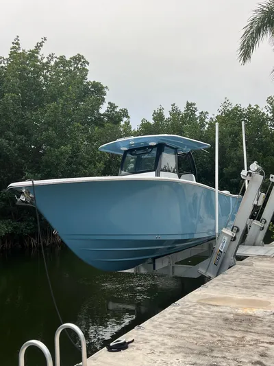 Yacht Photos Pics 2023 Sportsman Open 302 Center Console boat on lift by water, surrounded by trees.