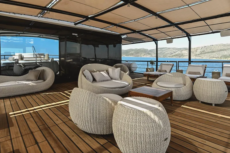 Chakra Yacht Photos Pics Luxurious yacht deck with modern wicker furniture, overlooking serene ocean and distant hills.