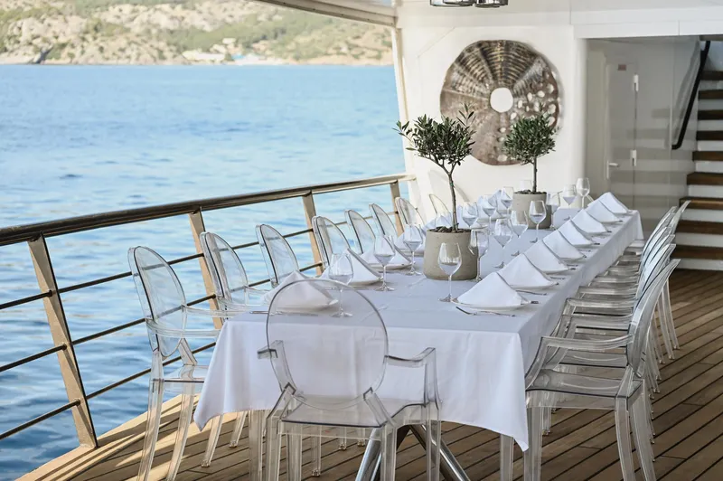 Chakra Yacht Photos Pics Elegant yacht dining setup with clear chairs, white tablecloth, and sea view on Devonport 86m, 1963.