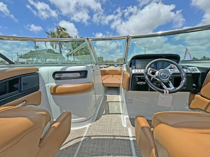 Yacht Photos Pics 2024 Crownline 290 XSS boat interior with tan seating, steering wheel, and clear skies.