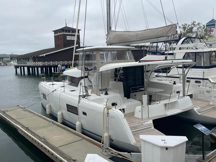 Hullchal Yacht Photos Pics 2021 Lagoon 42 catamaran docked at a marina, overcast sky, waterfront building in background.