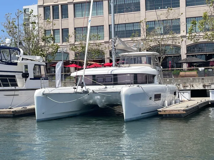 Hullchal Yacht Photos Pics 2021 Lagoon 42 catamaran docked at a marina, with modern buildings in the background.
