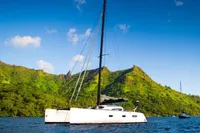 2005 Marsaudon Composites T 50 Catamaran sailing near lush green mountains under a clear blue sky.