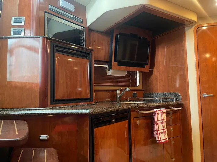 Knot Justified Yacht Photos Pics 2006 Sea Ray 38 Sundancer interior kitchen with wood cabinetry, appliances, and a mounted TV.