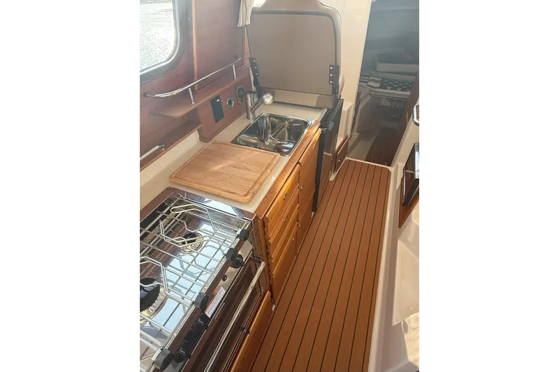Anima Gemella Yacht Photos Pics 2023 Ranger Tugs R-27 interior galley with stove, sink, and wooden cabinetry.