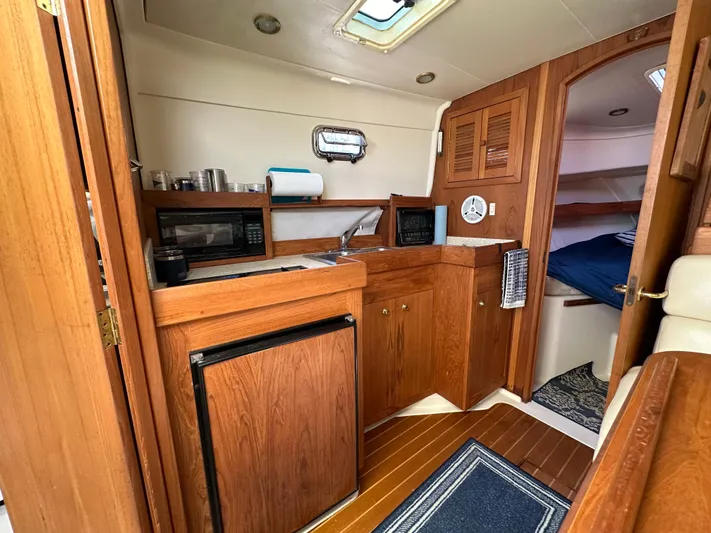  Yacht Photos Pics 2002 Mainship Pilot 34 interior with wood cabinetry, kitchenette, and cozy sleeping area.