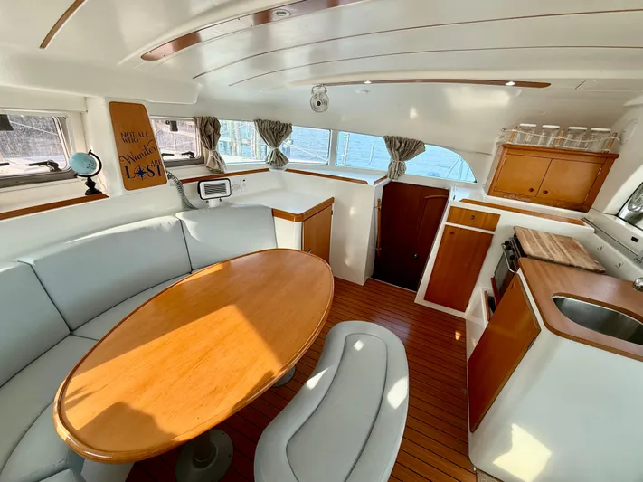 Wander Cat Yacht Photos Pics Interior of 2004 Lagoon 380 catamaran with wooden table, seating, and kitchenette.