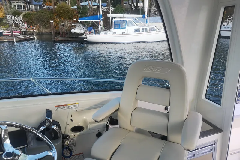  Yacht Photos Pics Interior view of 2016 Boston Whaler 315 Conquest Pilothouse with helm seat and waterfront backdrop.