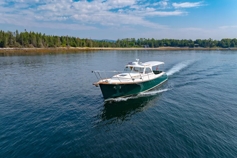 Genie Yacht Photos Pics 1999 Hinckley Picnic Boat cruising on a serene lake with forested shoreline.