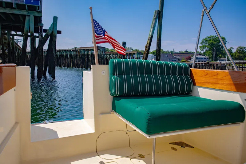 Genie Yacht Photos Pics 1999 Hinckley Picnic Boat with green seating, docked by wooden pilings, American flag waving.