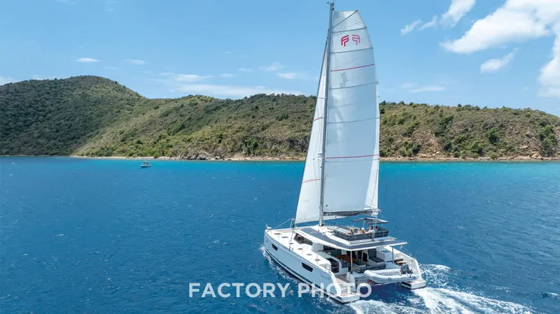 Bonova Yacht Photos Pics 2022 Fountaine Pajot Tanna 47 sailing in clear blue waters near a lush island.