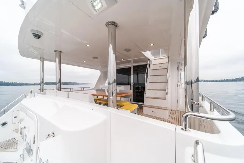 Smile Smile Smile Yacht Photos Pics 2022 Outer Reef 720 Motor Yacht deck with seating and stairs, overlooking calm waters.