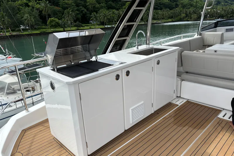  Yacht Photos Pics Outdoor kitchen on 2025 Aquila 54 Yacht with grill and sink, docked by lush greenery.