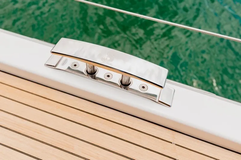 Dictador Yacht Photos Pics Deck cleat on 2022 Beneteau Oceanis Yacht 62, with teak flooring and green water background.
