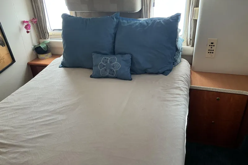 Ananda Yacht Photos Pics Cozy bedroom interior of 1999 Silverton 422 Motor Yacht with blue pillows and wooden cabinets.