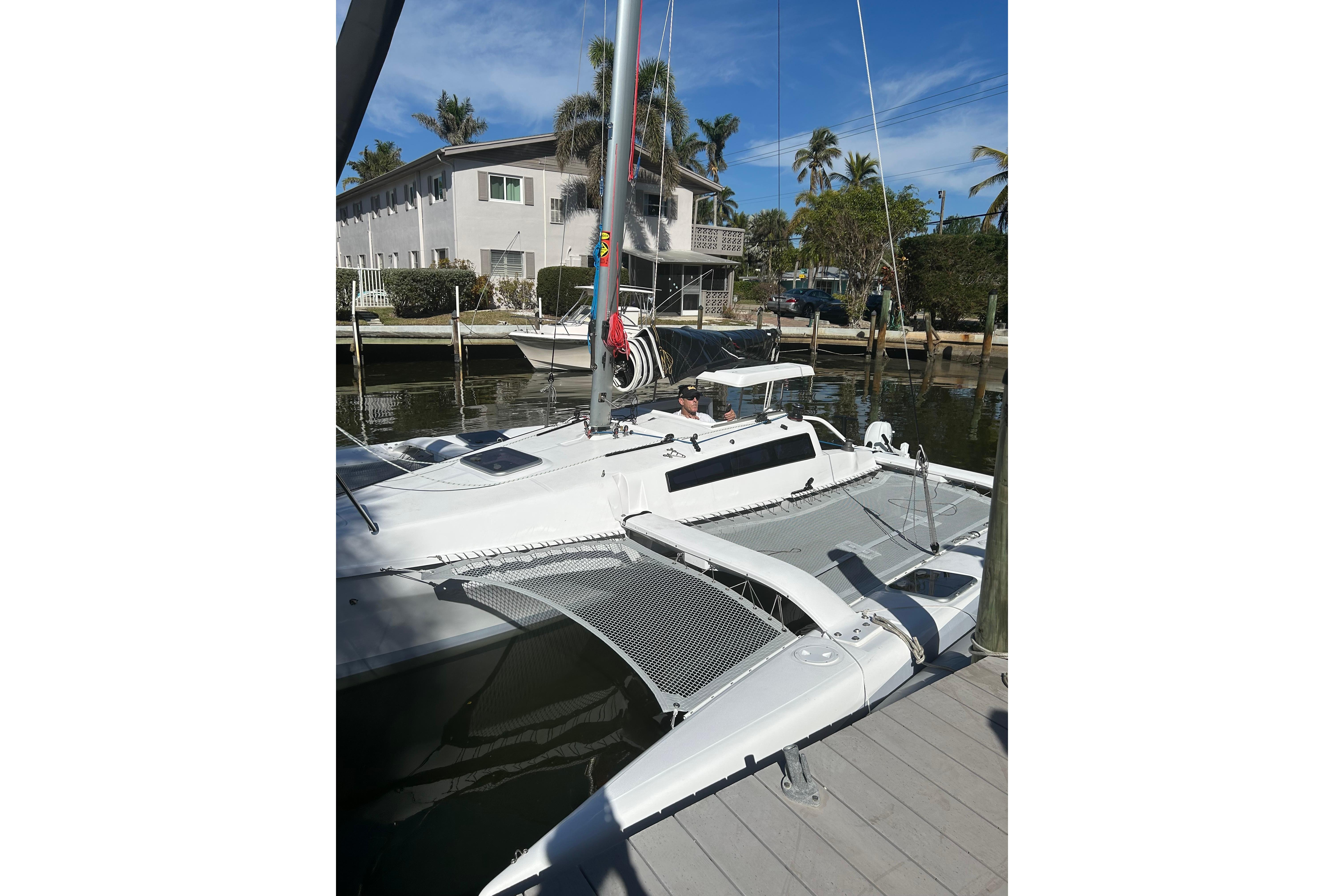 2025 Corsair 760 trimaran docked near waterfront homes, under clear blue skies.