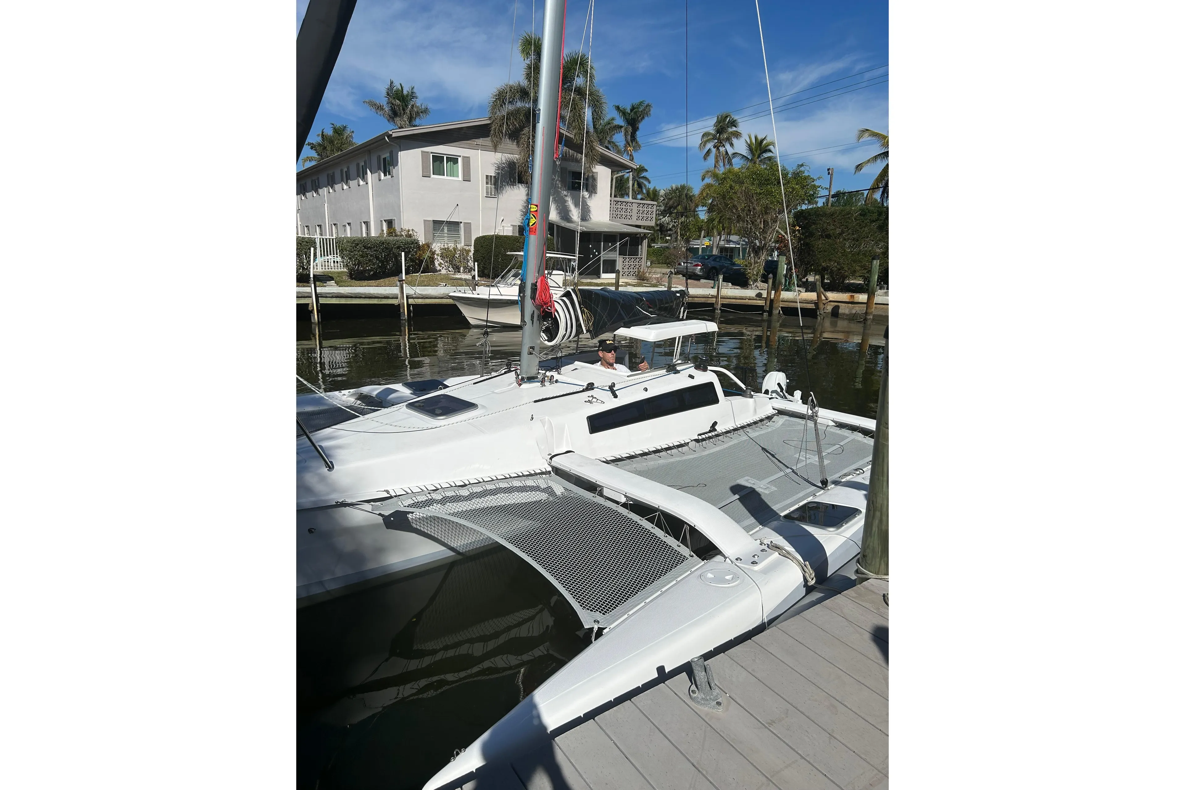 2025 Corsair 760 trimaran docked near waterfront homes, under clear blue skies.